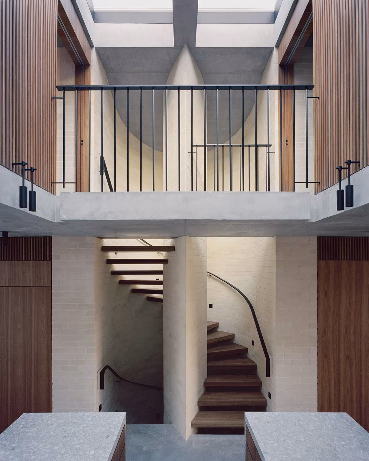 Patio interior de la Bronte House con escalera de madera de peldaños en voladizo y pasarela con barandilla negra