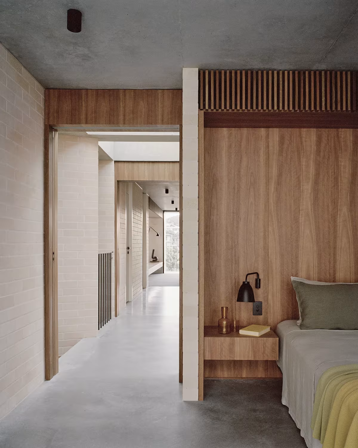 Dormitorio de la Bronte House abierto a un pasillo de ladrillo y madera con luz natural al fondo