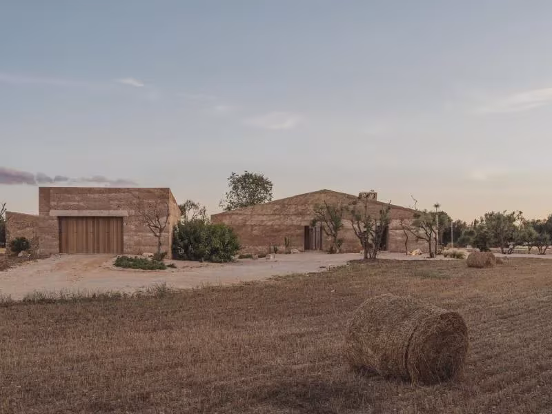 Casa Ca na Pau con muros de tierra y portón de madera entre los campos de cultivo, vista desde el camino