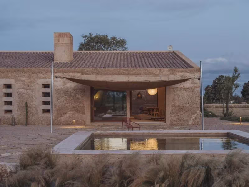 Casa Ca na Pau al anochecer con cubierta de teja, toldo curvo sobre el porche y piscina frente a la fachada