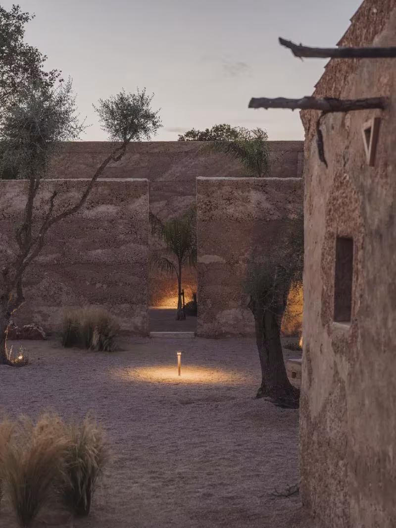 Patio de arena entre muros de tierra apisonada con luz baja y olivos al caer la tarde en la casa Ca na Pau