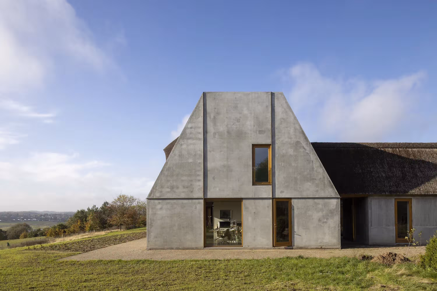 Testero de hormigón con ventanas de madera junto a la cubierta de paja de Åstrup Have
