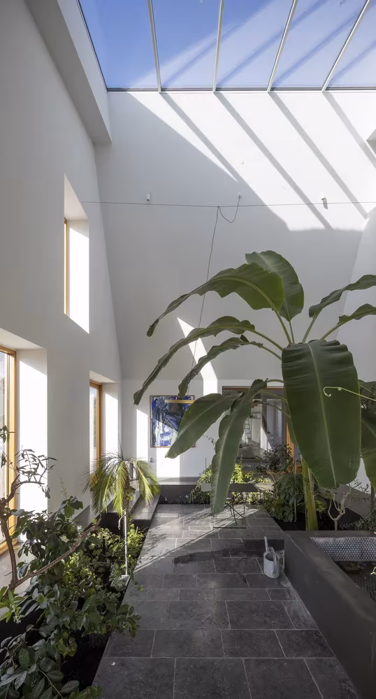 Espacio con lucernario, plantas y suelo de pizarra entre muros blancos en la granja Åstrup Have