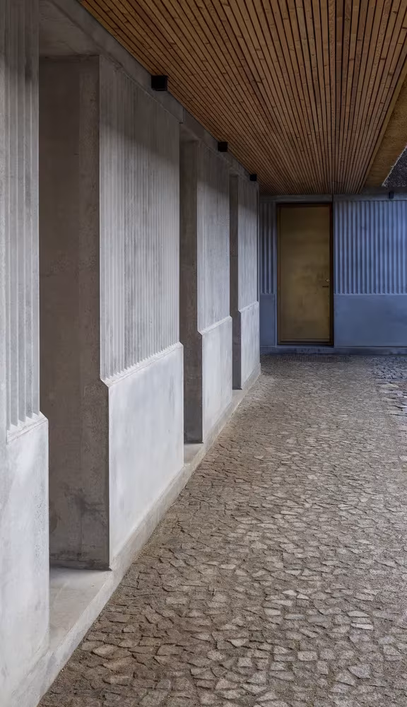Galería con pilastras de hormigón acanalado, adoquines y techo de madera en Åstrup Have