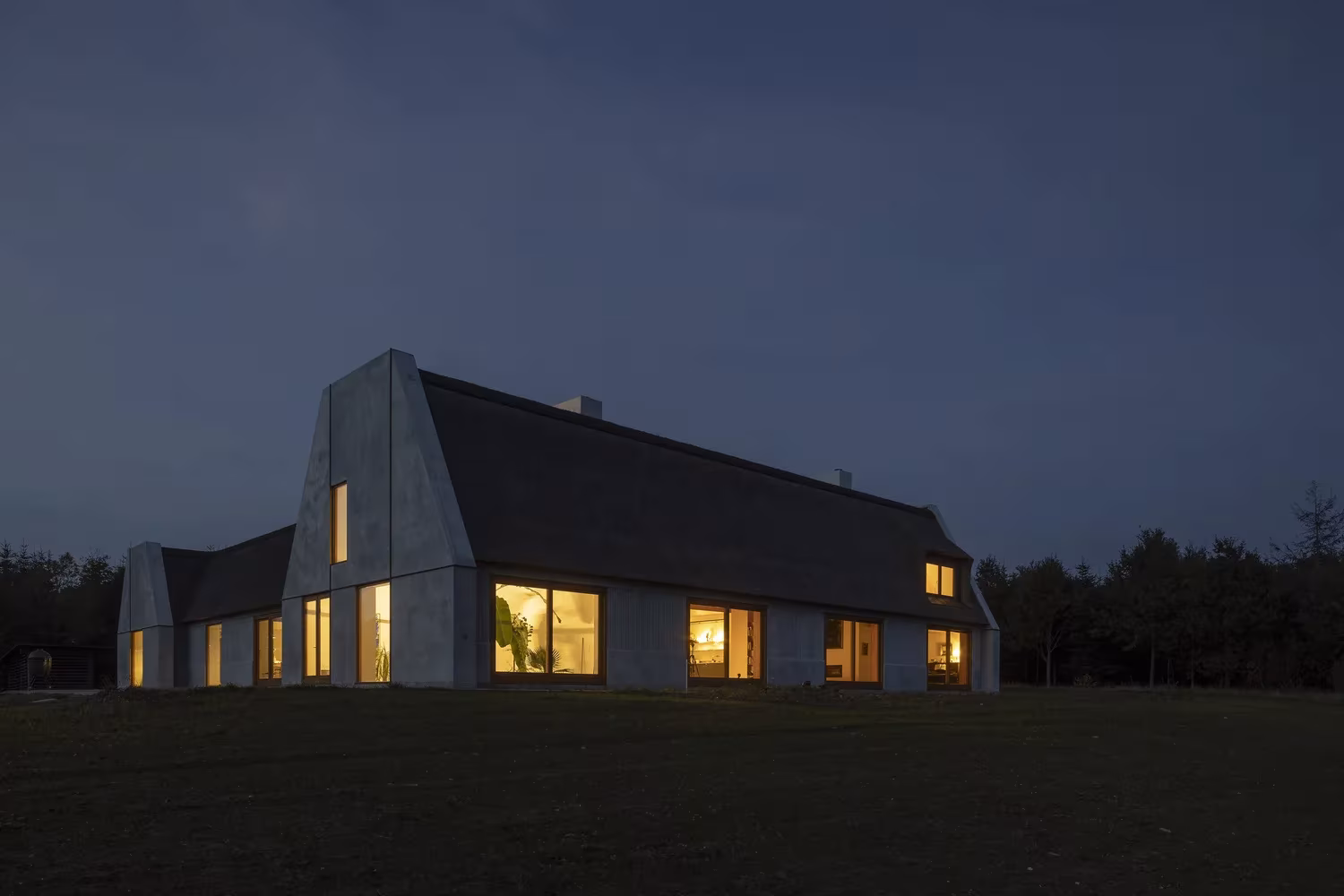Åstrup Have al anochecer, con las ventanas iluminadas bajo la cubierta de paja