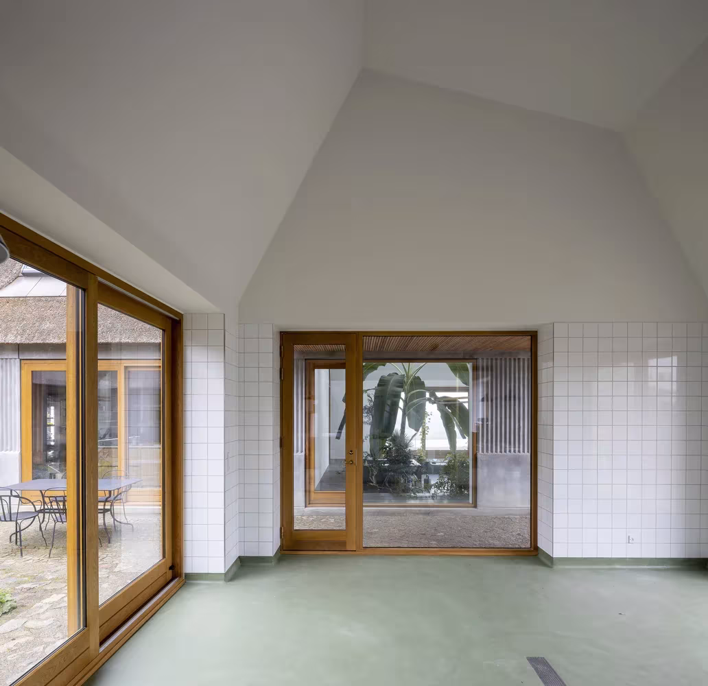 Sala de paredes blancas alicatadas y suelo verde con ventanal al patio en Åstrup Have