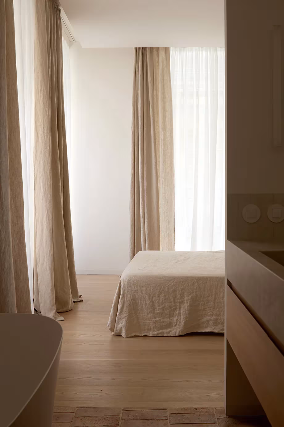 Dormitorio con cortinas de lino y tarima clara visto desde un paso entre muebles de madera, en Valencia