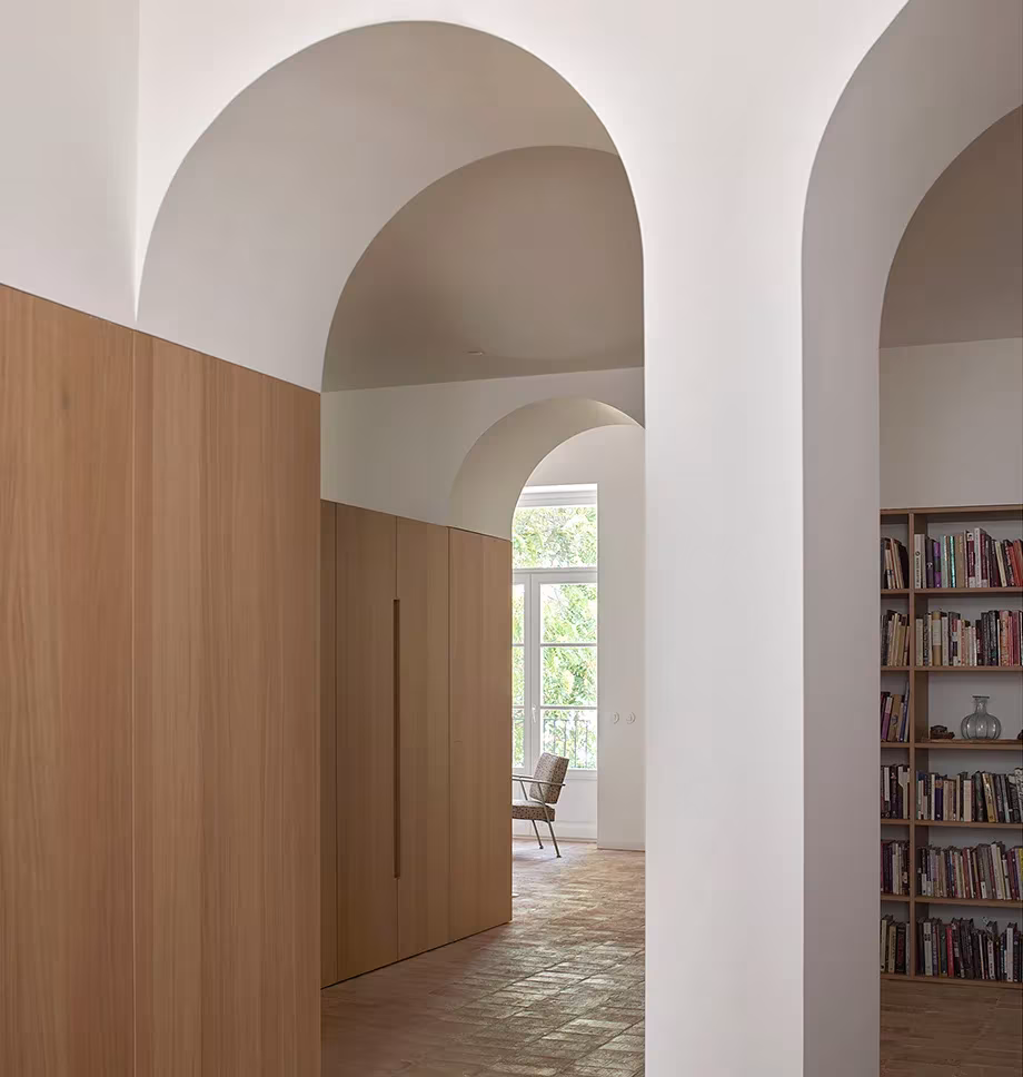 Arcos de yeso blanco que enmarcan paneles de roble y una biblioteca al fondo, en la vivienda de Valencia