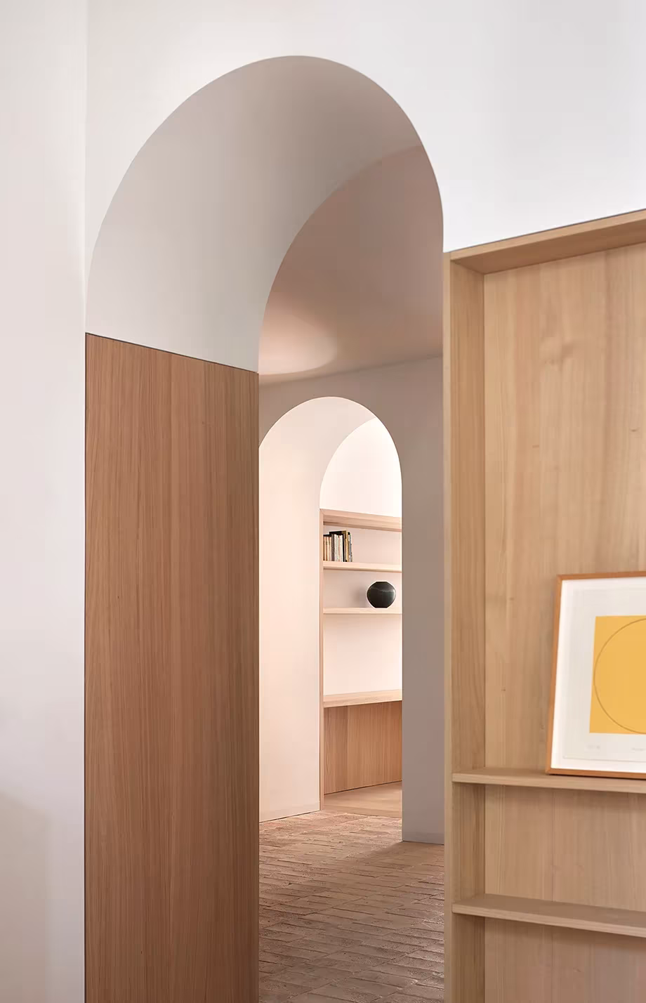 Perspectiva de arcos encadenados con paneles de madera y estantes en la vivienda de Valencia