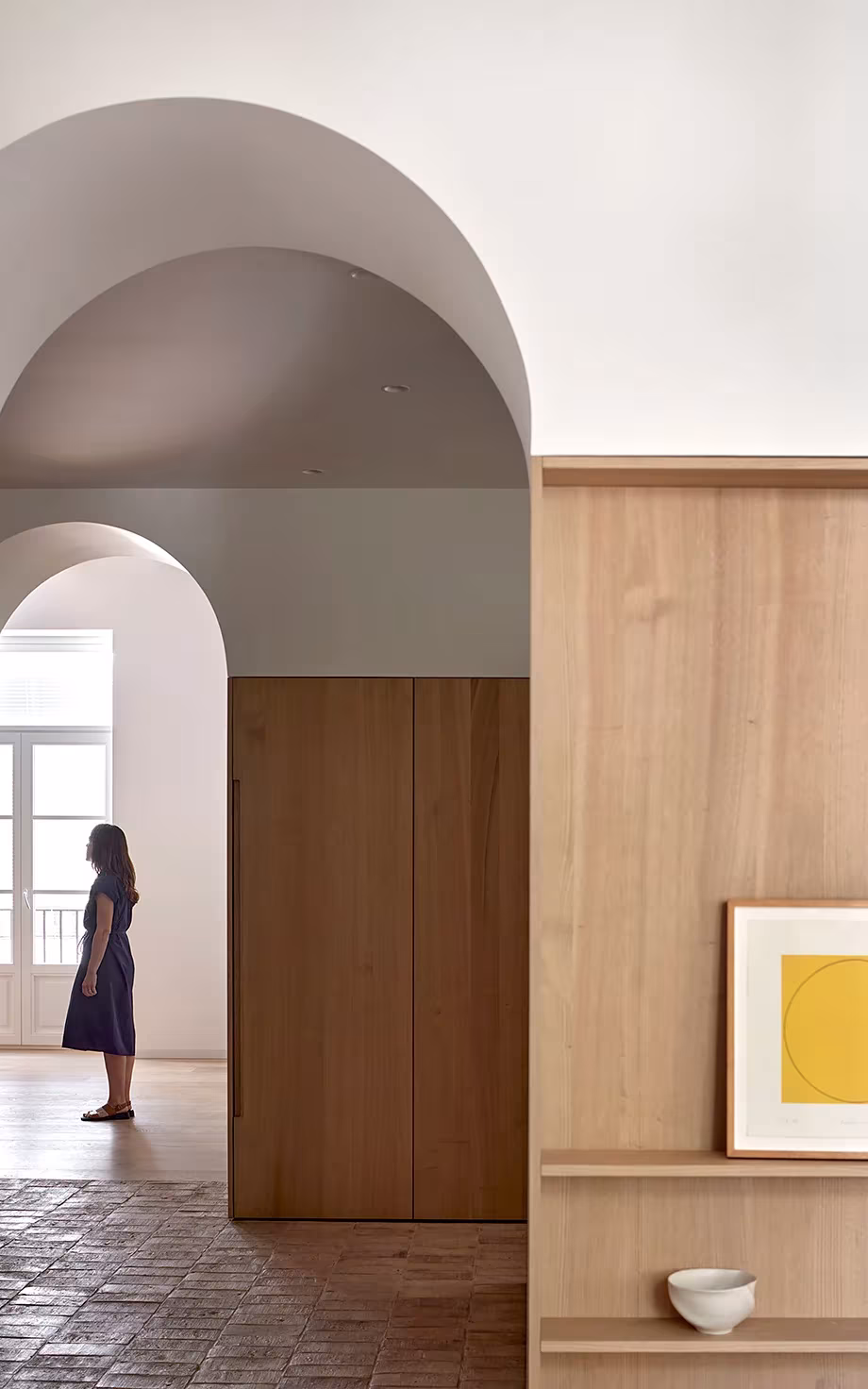 Mujer ante un arco de yeso y un mueble de roble con una pintura amarilla en la vivienda de Valencia