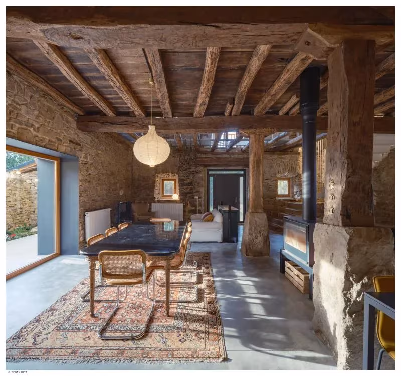 Comedor de Garaitia Etxea con mesa oscura, alfombra y estructura de madera original bajo la cubierta