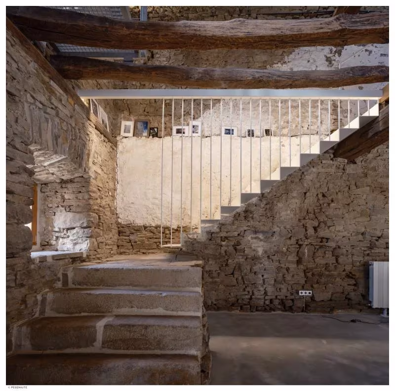 Escalera de obra y muros de piedra vistos en el interior de Garaitia Etxea, con barandilla blanca en lo alto