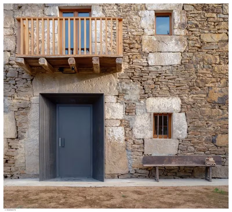 Fachada de piedra de Garaitia Etxea con balcón de madera, ventanas pequeñas y puerta metálica oscura