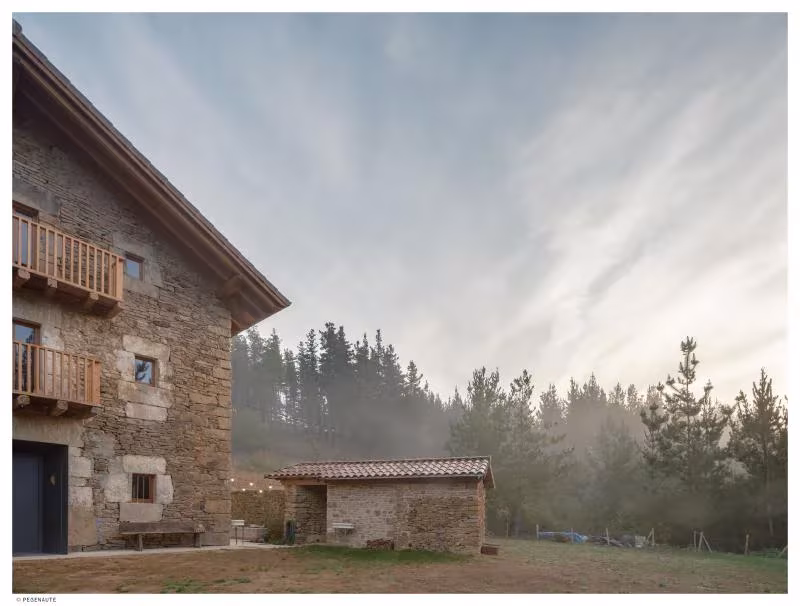 Garaitia Etxea al amanecer, con balcones de madera sobre el muro de piedra y un cobertizo anejo entre pinos