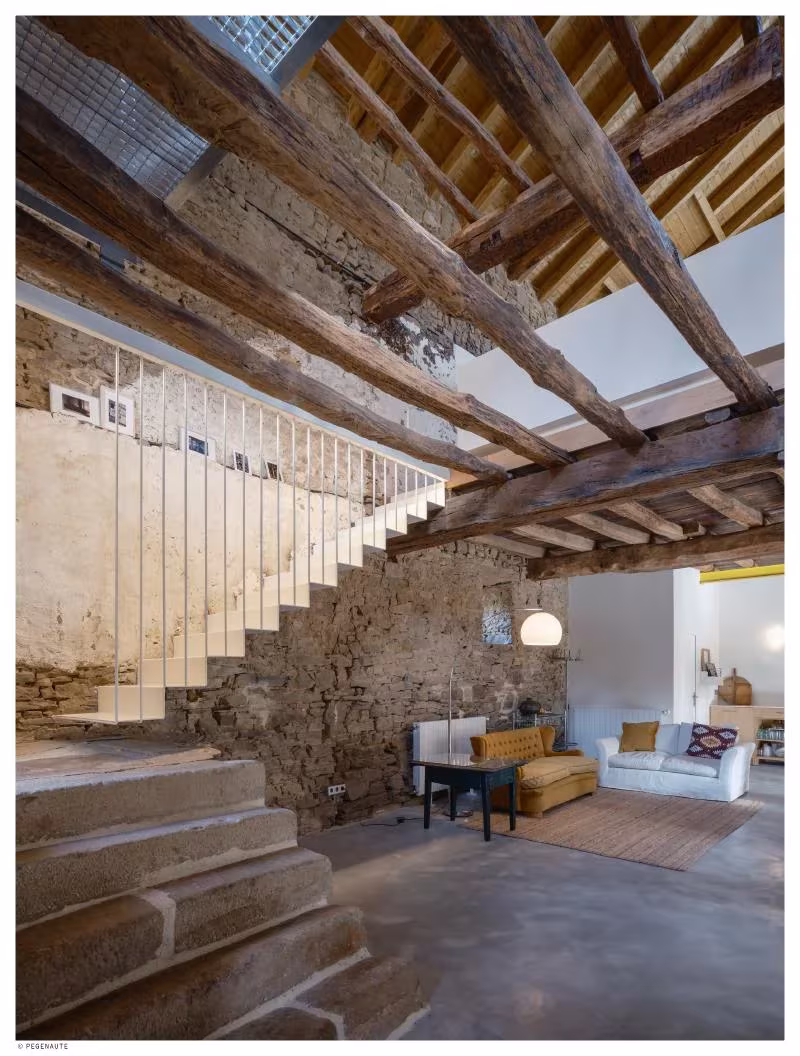 Escalera blanca junto a un muro de piedra y un salón con sofás, bajo las vigas de Garaitia Etxea