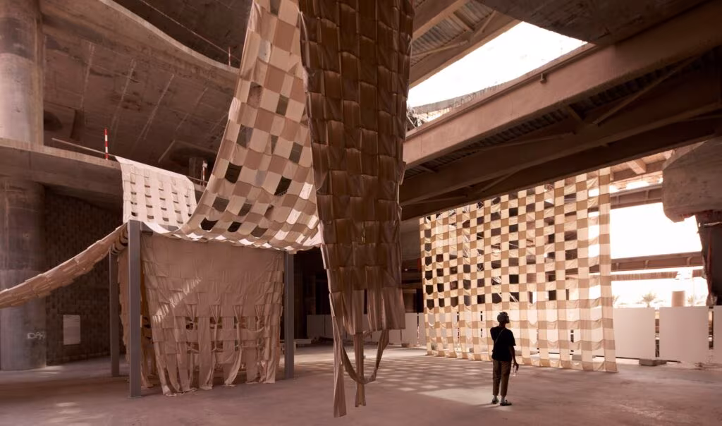 Instalación textil de tiras tejidas que cuelga en un edificio de hormigón inacabado en Sharjah, Super Limbo