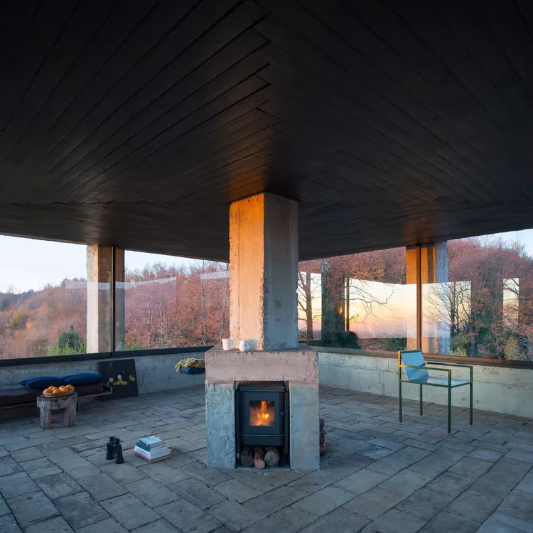 Interior del Pabellón ROSA con chimenea de hormigón central, techo oscuro de madera y vistas panorámicas