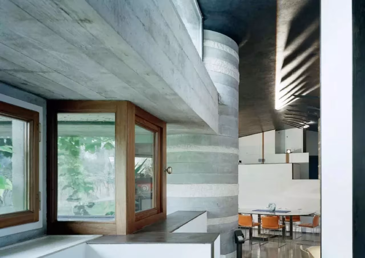 Interior de la Villa Ottolenghi con hormigón visto, ventana esquinera de madera y comedor al fondo