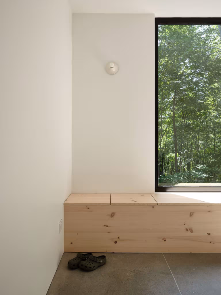 Lidded pine bench under a tall black-framed window at the entrance of TISSARAOUATA