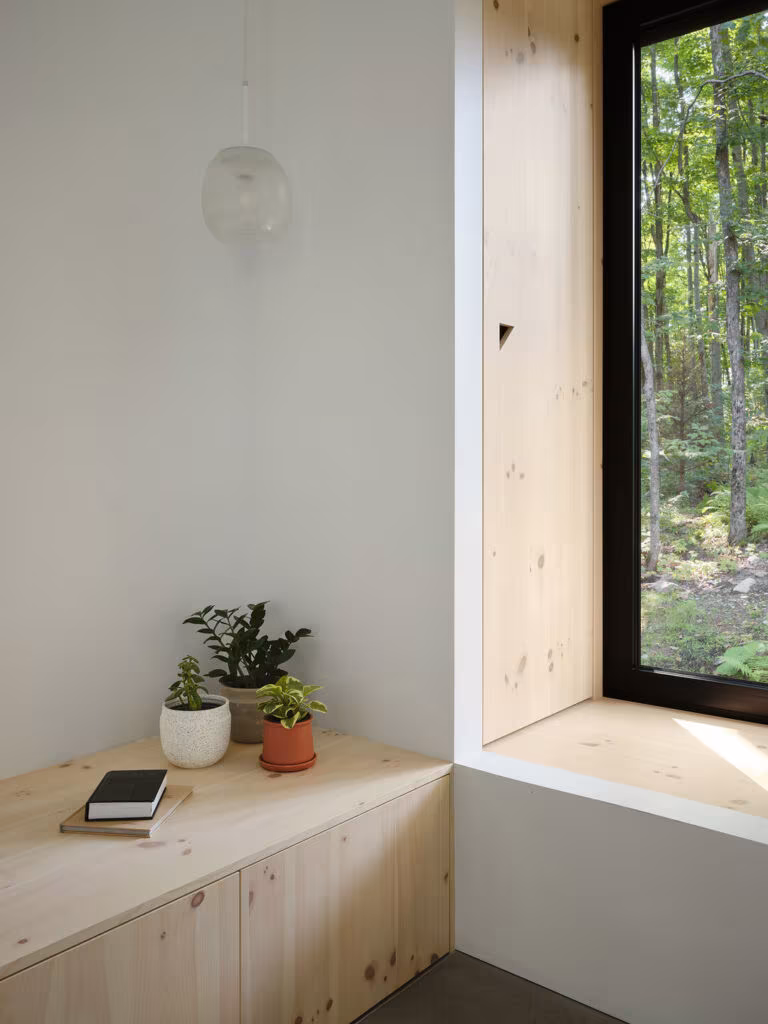 Pine window seat with plants and books beneath a black-framed window, TISSARAOUATA