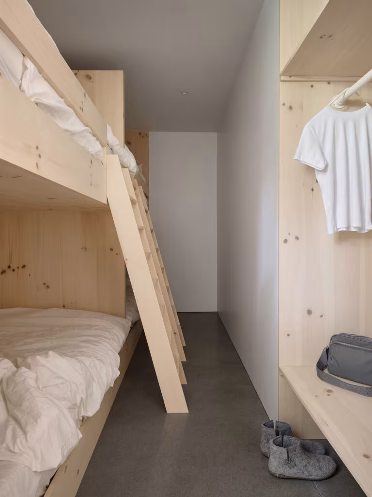 Pine bunk bed with a ladder and open wardrobe in a narrow bedroom, TISSARAOUATA