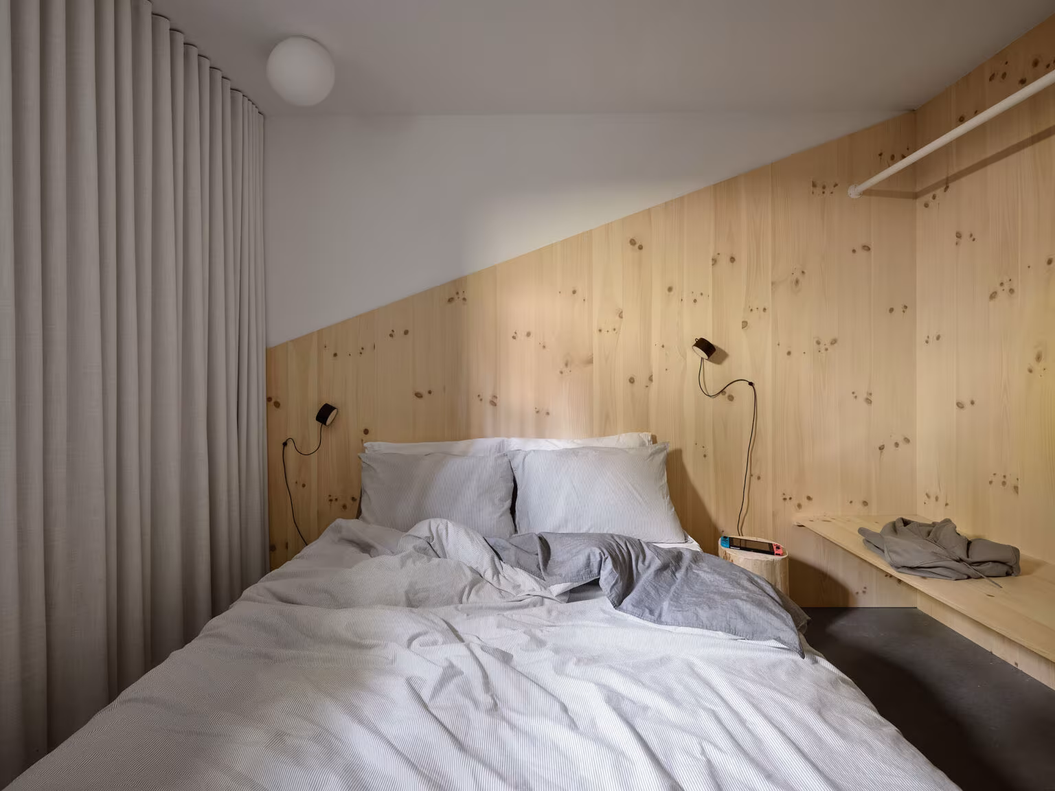 Pine-lined bedroom with a long curtain, rumpled bed and continuous shelf, TISSARAOUATA