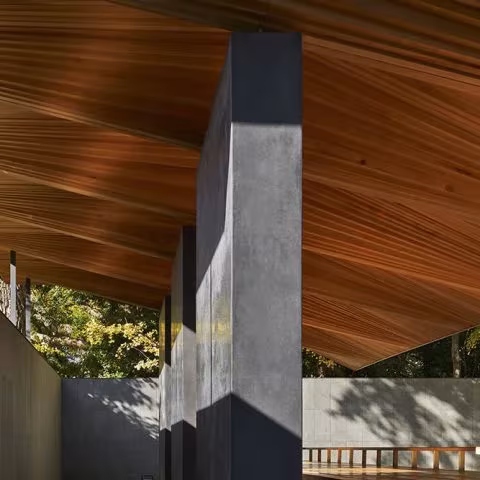 Pilares oscuros y cielo de lamas de madera en el pabellón de Ueno Toshogu, con el muro de piedra detrás
