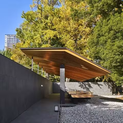 Pabellón de Ueno Toshogu con cubierta de madera volada y un muro gris, entre árboles de otoño