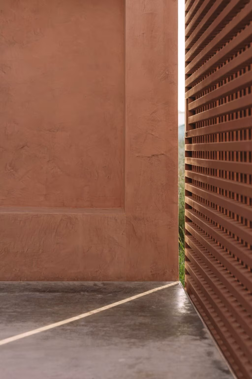 Vertical timber screen beside a red lime wall and a concrete floor at Casa Plaj