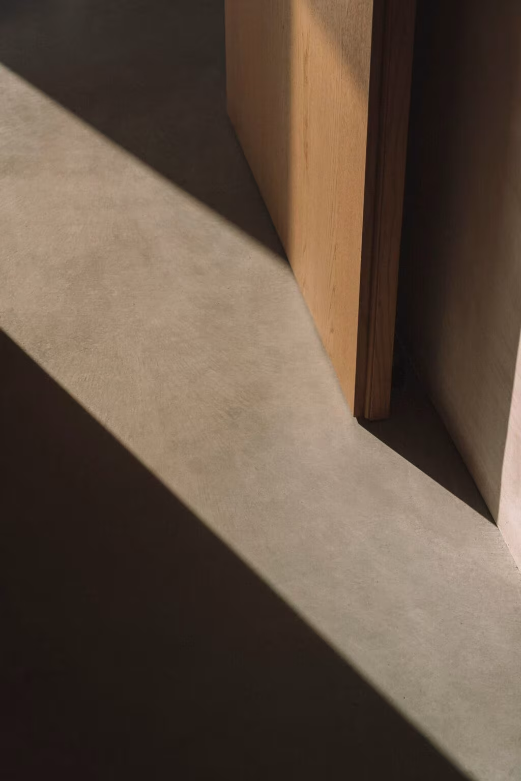 Raking shadow across the plaster floor and a timber door leaf in Casa Plaj