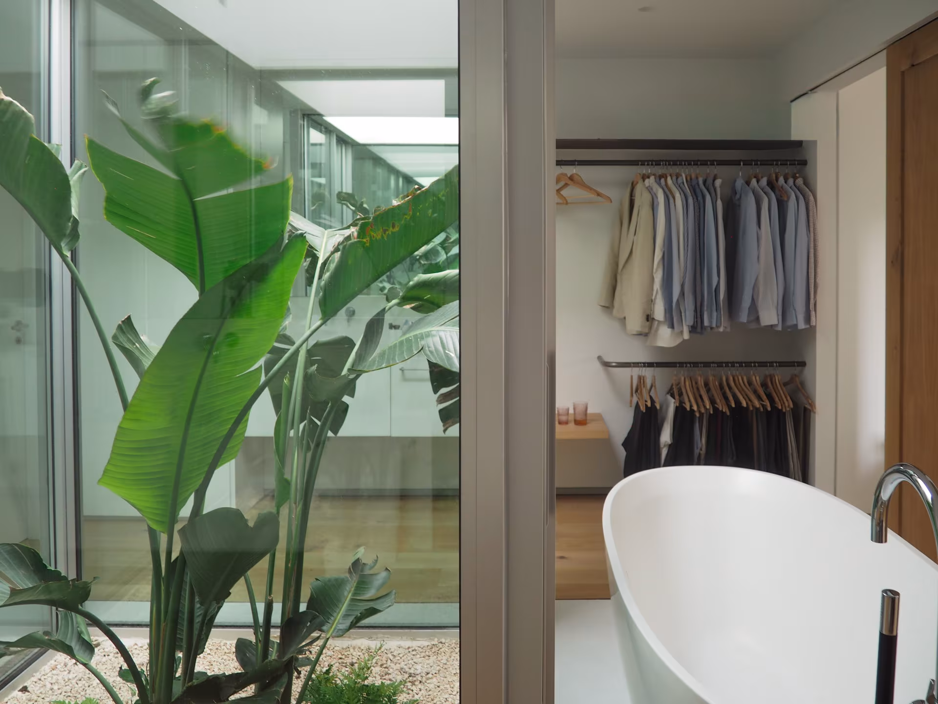 Vestidor con bañera exenta y strelitzia tras una cristalera sobre un patio en la Casa de los arces