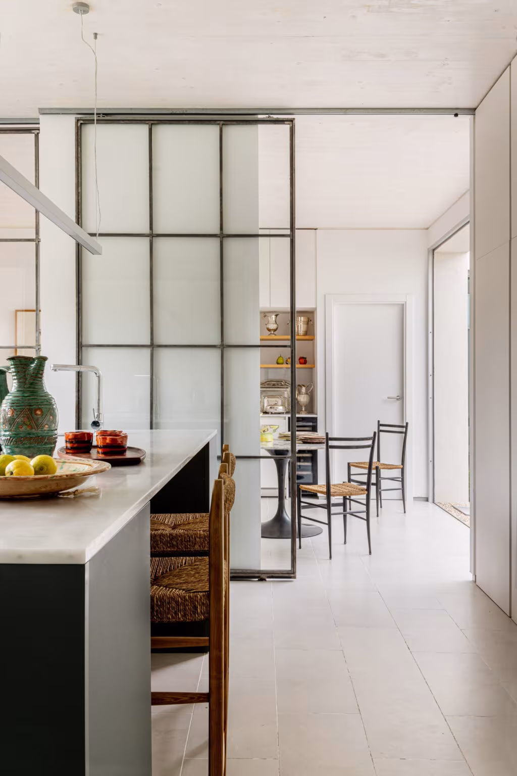 Cocina con isla y puerta corredera de vidrio y perfiles negros abierta al comedor en la Casa de los arces