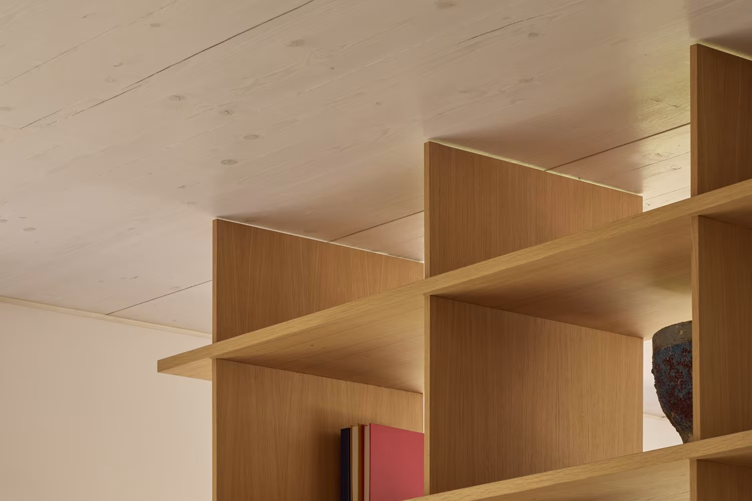 Detalle de estantería de roble con baldas inclinadas bajo un techo de madera clara en el Proyecto AB
