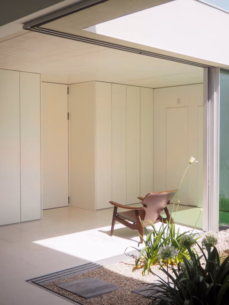 Sala abierta a un patio con puertas empotradas blancas, butaca de cuero y suelo claro en el Proyecto AB