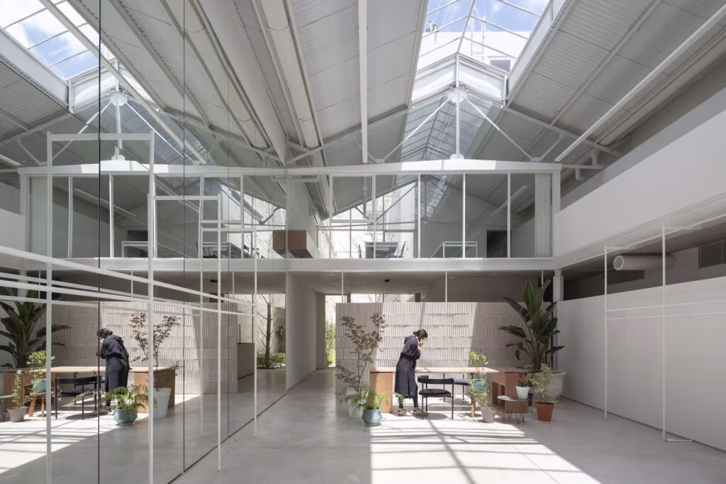 Nave luminosa de NICETO con cubierta de cerchas blancas y lucernarios, entresuelo acristalado y mesas de trabajo