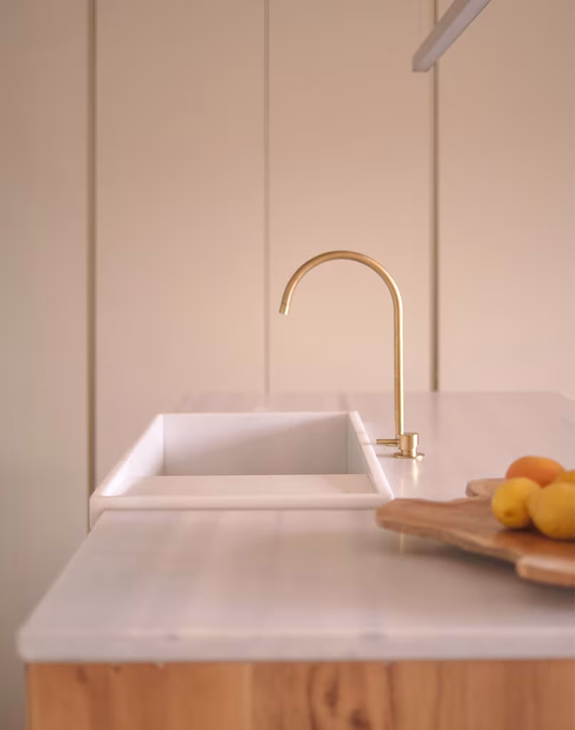 Pale stone sink with brass tap and white worktop on a timber island in the La Vera kitchen