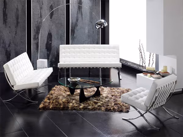 White Barcelona chairs and sofa with a Noguchi glass table and a fur rug in a dark living room