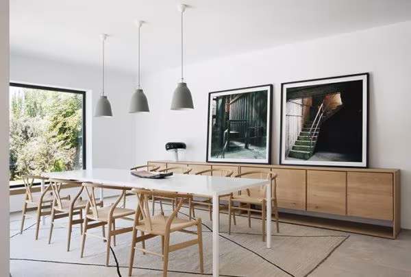 Dining room with a long white table, timber Wishbone chairs, an oak sideboard and grey pendant lamps