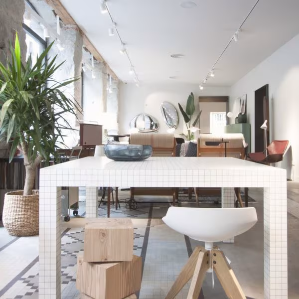 White-tiled Quaderna table with a stool and timber blocks in a space with plants and track lighting