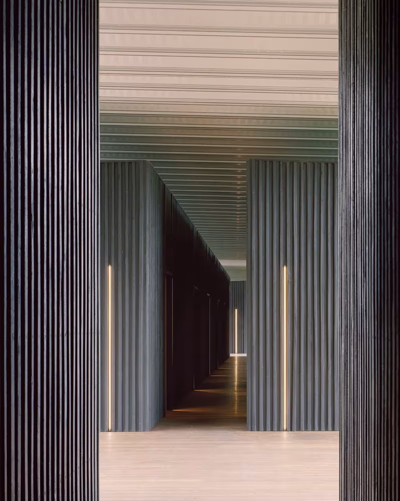 Corredor de alojamiento en Bundanon con paneles verticales de madera oscura y luz lineal entre las puertas