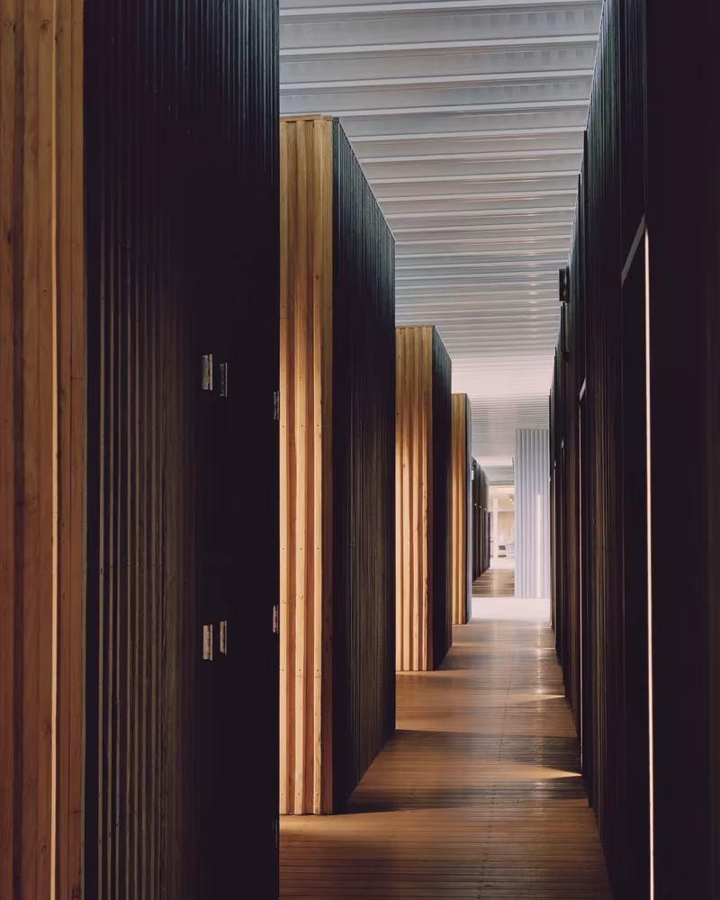 Pasillo de las habitaciones de Bundanon con lamas de madera quemada y listones de madera clara