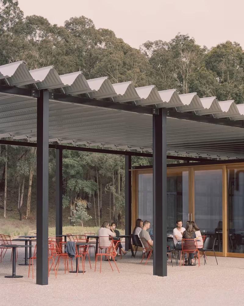Porche con cubierta metálica plegada y mesas de café bajo los eucaliptos en el Bundanon Art Museum