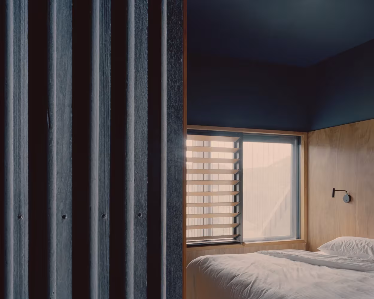 Dormitorio de Bundanon con ventana de lamas, revestimiento de madera clara y celosía de madera oscura