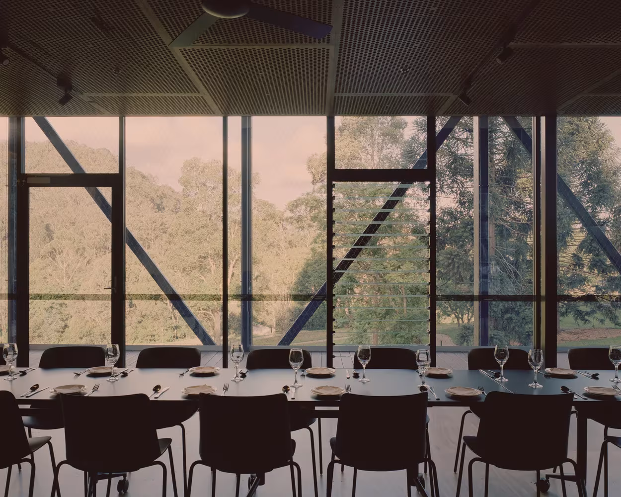 Comedor largo del Bundanon Art Museum con mesa corrida y vistas al bosque a través de la fachada de acero y vidrio