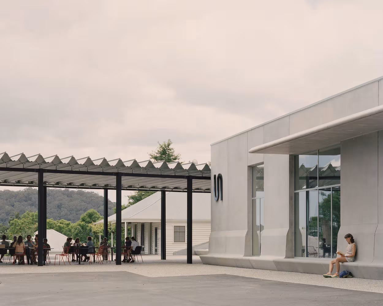 Patio del Bundanon Art Museum con porche de acero junto a un volumen de hormigón claro y gente sentada