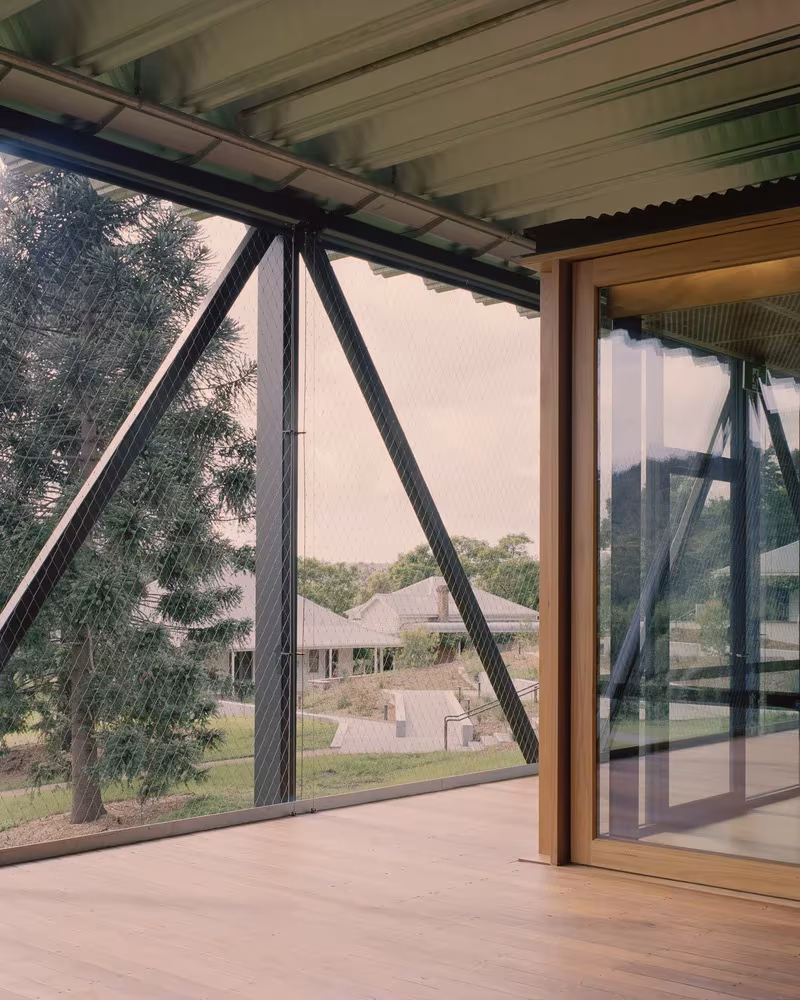 Interior de madera con muro cortina de acero y puerta corredera de madera abierto a los jardines de Bundanon