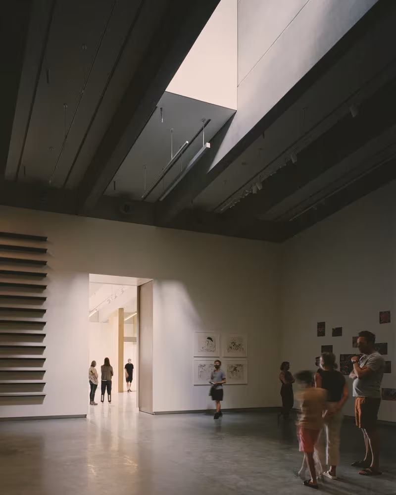 Sala de exposición del Bundanon Art Museum con lucernario, vigas de acero oscuro y visitantes ante los dibujos