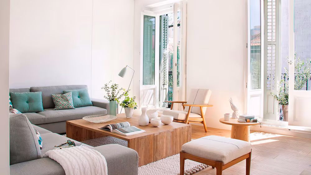 Living room with grey sofas, a low timber table and a pouf beside a balcony, in an Ábaton project in Madrid