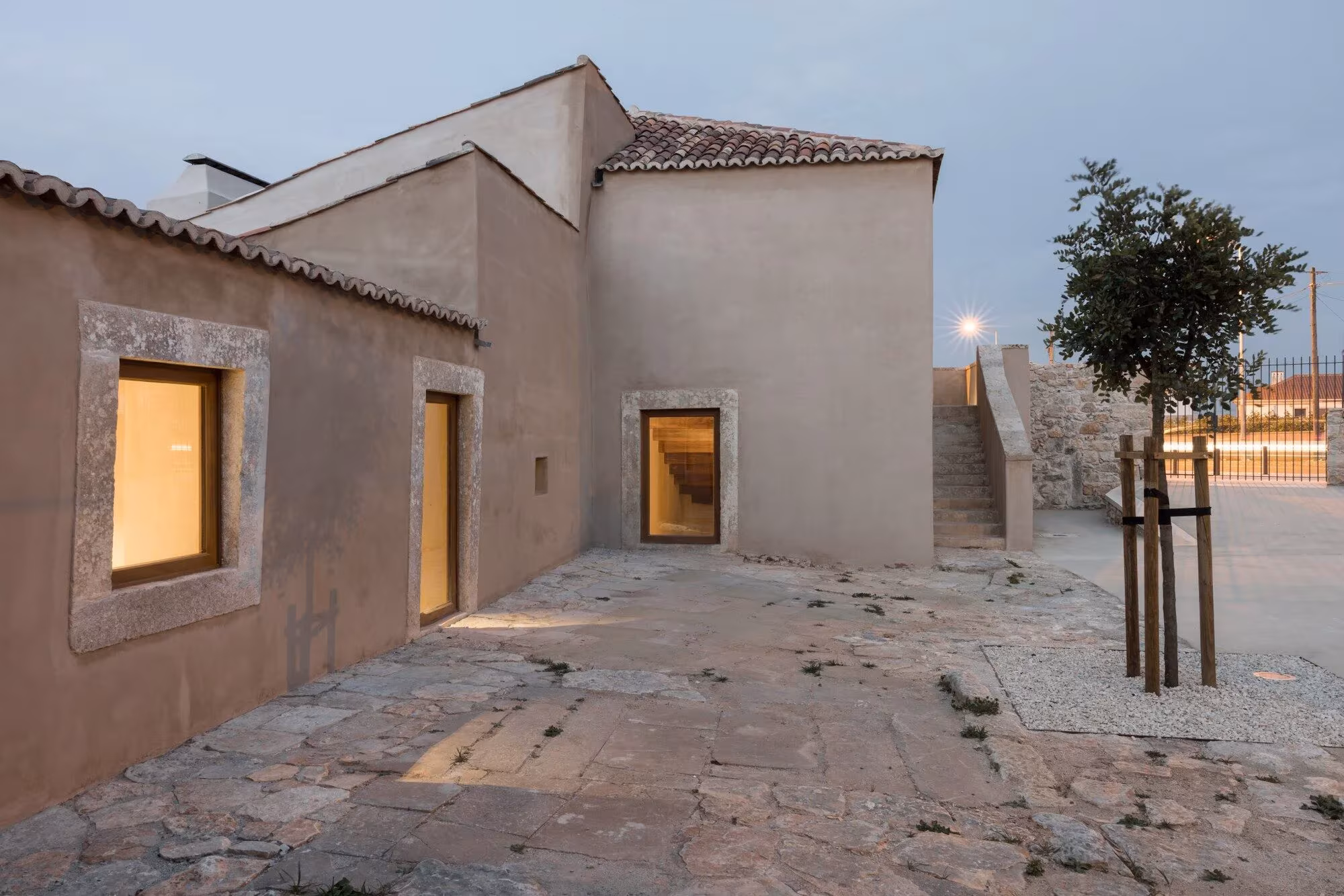 Fachada encalada del Casal Saloio con huecos de piedra iluminados al atardecer sobre el pavimento pétreo