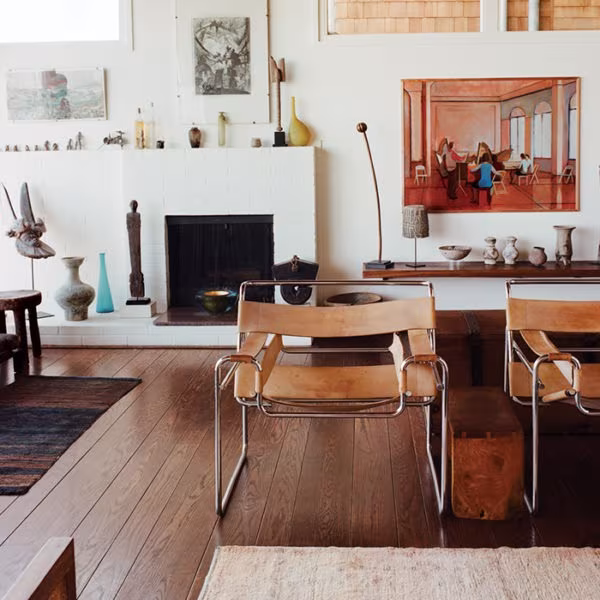 Pale leather Wassily armchairs before a white fireplace in a living room with a timber floor and ceramics